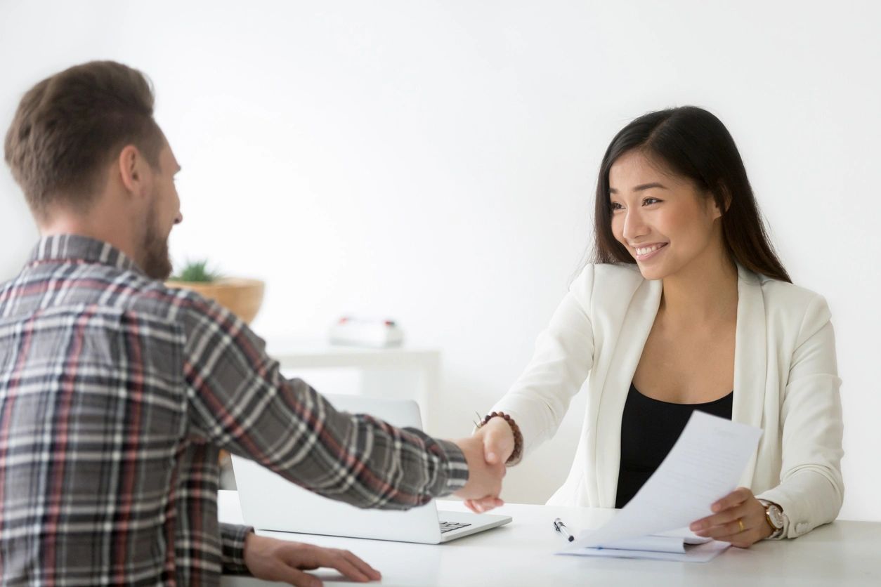 A man and woman shaking hands over papers.